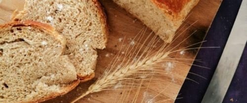 Sliced whole wheat bread on a wooden board with wheat stalks and a knife, perfect for baking and food photography.