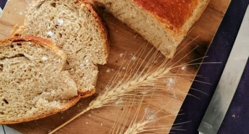 Sliced whole wheat bread on a wooden board with wheat stalks and a knife, perfect for baking and food photography.